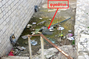 Στάσιμο ακάθαρτο υγρό και σκουπίδια γύρω από το φρεάτιο αποχέτευσης (βλέπε βέλος) που δεν λειτουργεί αποχετευτικά, αλλά σαν εστία μόλυνσης.