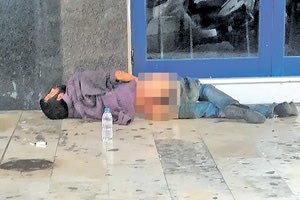 Ένας άνθρωπος πεσμένος στο έδαφος, αβοήθητος, με κατεβασμένα τα ρούχα του έξω από τον κινηματογράφο Αστόρια