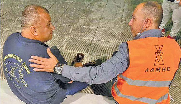 Ο εργαζόμενος του ΑΔΜΗΕ, όπως φαίνεται στην σχετική φωτογραφία, δίνει στον πυροσβέστη τα άρβυλά του γιατί τα δικά του είχαν λιώσει στη φωτιά.