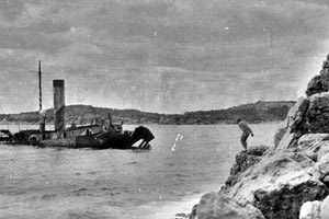 ΦΩΤΟΗΜΕΡΑΣ: Με φόντο ένα μισοβυθισμένο συμμαχικό πλοίο, ένας Γερμανός στρατιώτης ετοιμάζεται να βουτήξει από τα βράχια στον κόλπο της Σούδας. Πιθανότατα 1941. -ebay.