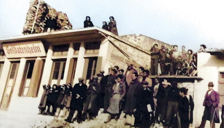 Μάιος 1944. Η πλατεία Μεϊντάνι του Καστελλίου με το «Soldatenheim» των Γερμανών. Οι κάτοικοι παρακολουθούν την αποχώρηση του Διοικητή Τροστ από το Καστέλλι. Αριστερά διακρίνεται ένας από τους ενετικούς πύργους του Καστελλίου