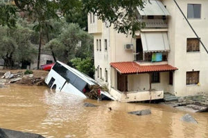Στις φωτογραφίες, όπως μεταδίδει η ΕΡΤ, απεικονίζεται μία τριώροφη κατοικία να έχει πάρει κλίση και να «στηρίζεται» σε ένα τουριστικό λεωφορείο που παρασύρθηκε και βρέθηκε στην αυλή, ενώ ο δρόμος μπροστά από το σπίτι έχει διαλυθεί από τα ορμητικά νερά.