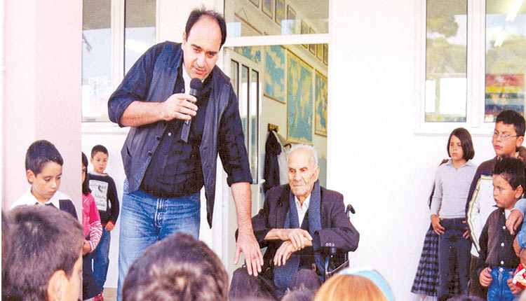 Οκτώβριος 2006. Ο ανάπηρος πολέμου (παγόπληκτος) Γεώργιος Χαραλαμπάκης στο Δημοτικό Σχολείο Καστελλίου, συνομιλεί με τον δάσκαλο Γεώργιο Καλογεράκη και μαθητές της ΣΤ΄ τάξης