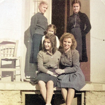 Καστέλλι, 1943. Στον εξώστη του σπιτιού του καθηγητή Παπαδάκη που το χρησιμοποιούσε ως κατοικία ο ταγματάρχης Τροστ, (Διοικητής του αεροδρομίου Καστελλίου). Όρθια δεξιά η οικιακή του βοηθός Ασπασία Παπουτσάκη. Δίπλα της στέκεται το παιδί της, η μικρή Μαρία.